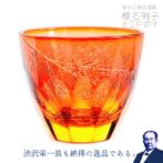 グラスにお酒を入れるとグラス底面に彫刻した模様が側面に映り込み赤く染まる紅葉が広がる、砂切子ならではの不思議なグラスです。 オレンジの素地に鮮やかな金赤を被せた2重構造の被せ硝子を使用し、側面では赤く染まった紅葉が最後の輝きを見せ、お酒を注ぐと底面の紅葉が側面に映り込み紅葉が舞い落ちる様子を表現しています。